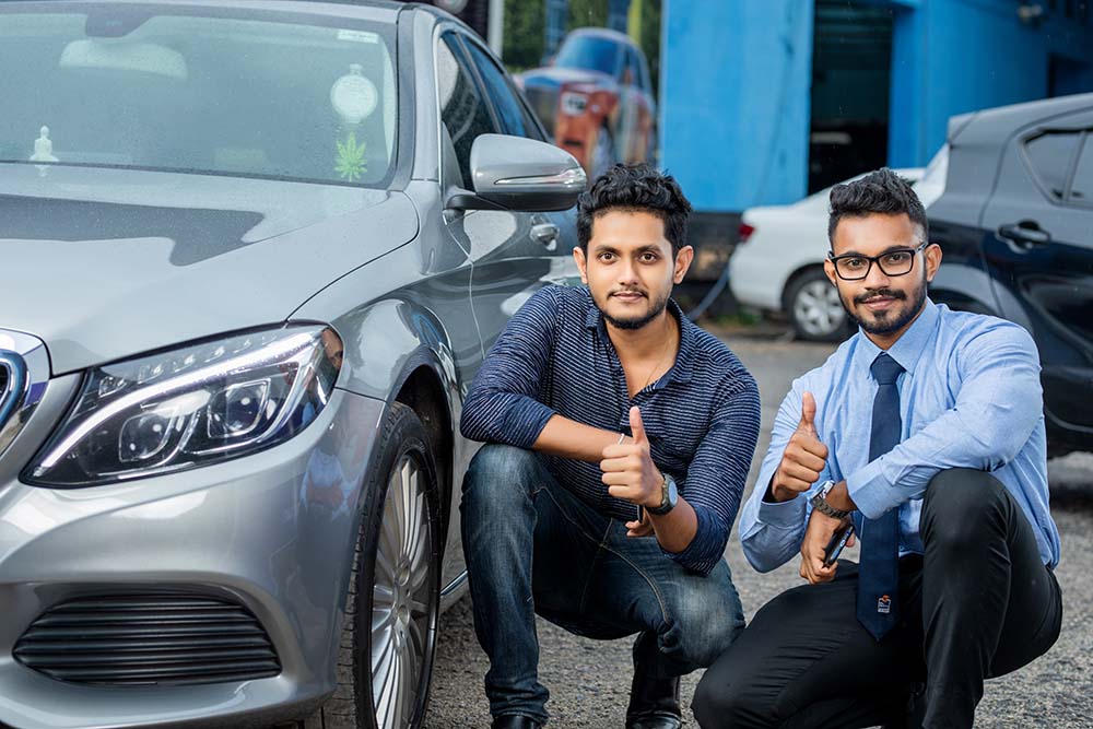 Two younge men posing beside a car at Mr. Paint Auto